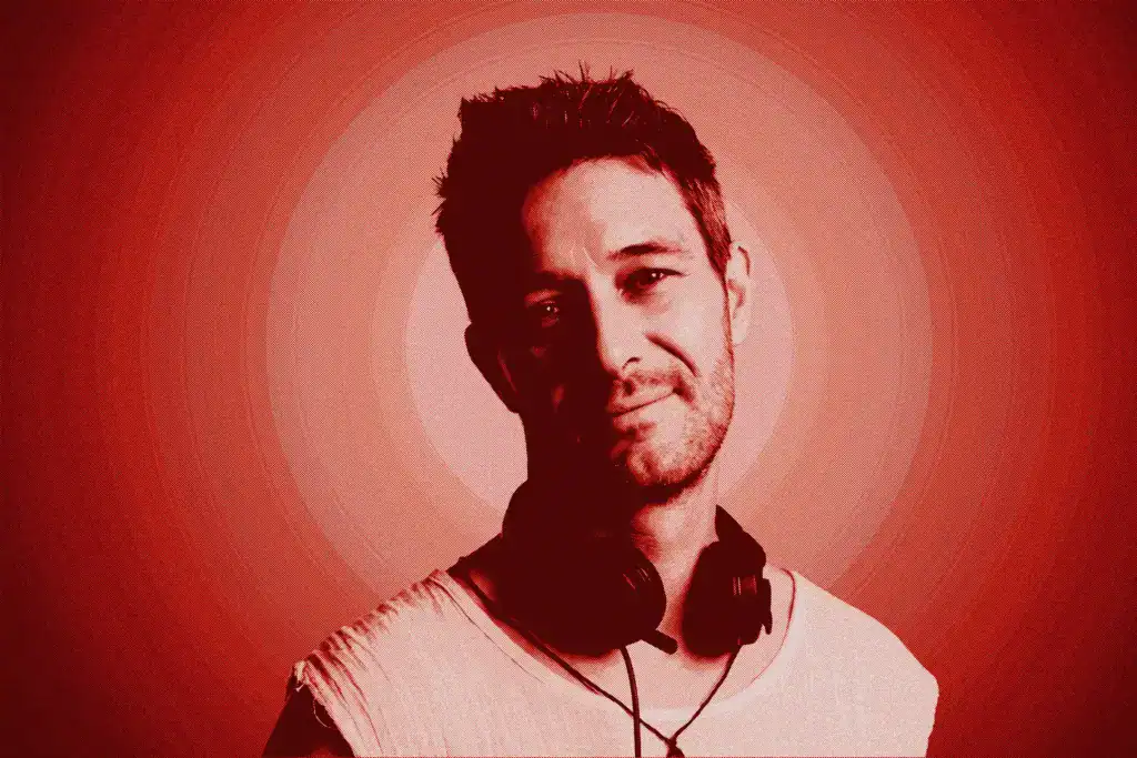 TOM BASTA, a DJ and music artist, wearing headphones, smiling against a red background.