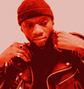 Portrait of a man in a red beanie and leather jacket, looking down thoughtfully.